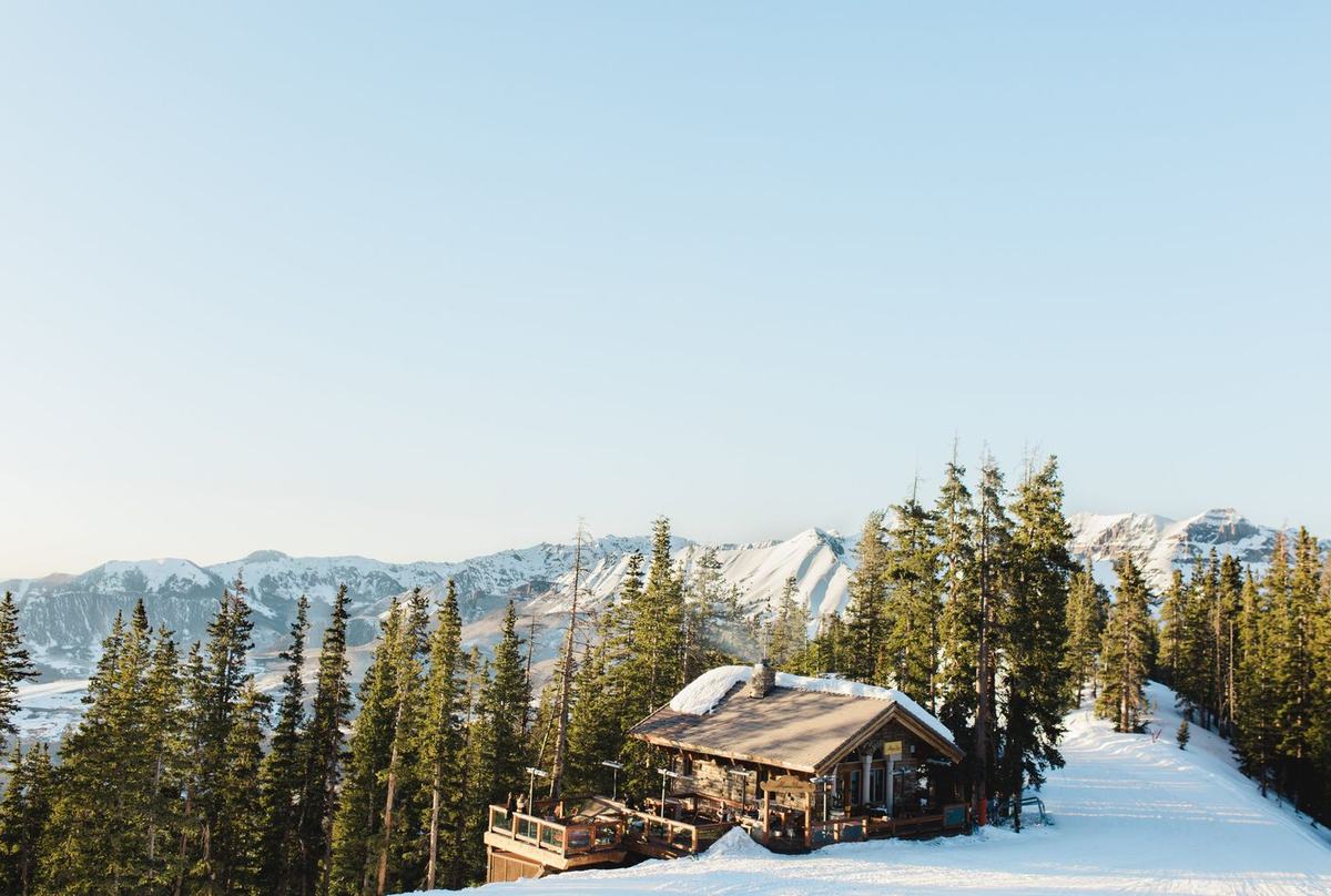 Alpino Vino seen from across the See Forever run in winter sun, the chalet and its deck among the pines with the San Juan peaks behind