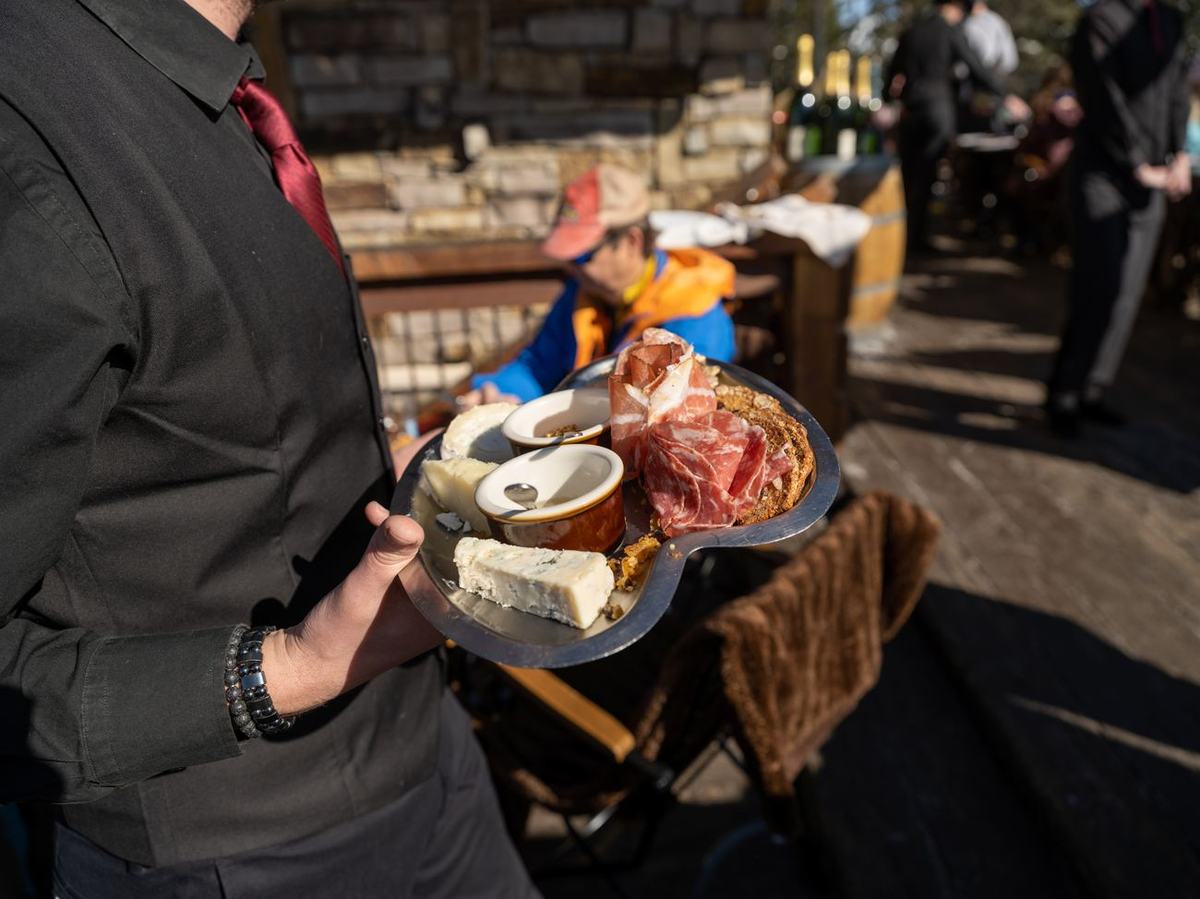 A server carrying a board of cured meats, Italian cheeses, honey and mustard out to the sunlit deck at Alpino Vino, Telluride