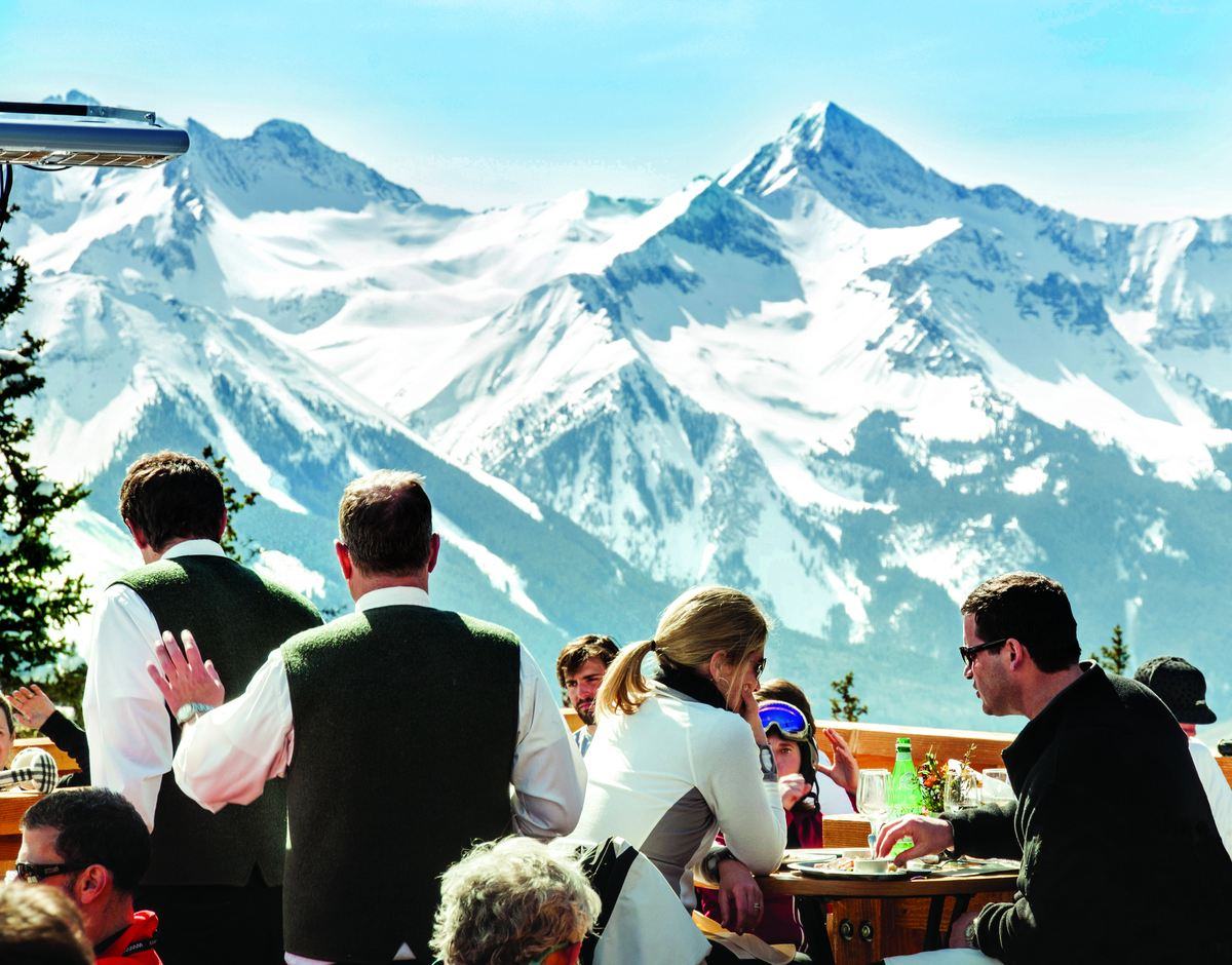 Guests eating lunch on the deck at Alpino Vino with the snow-covered Wilson Range filling the view behind, 11,966 feet above Telluride