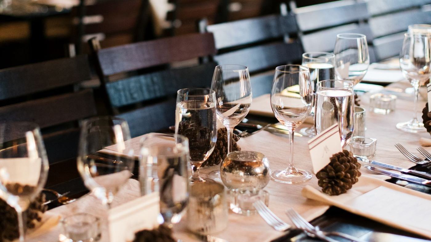 A private event table set at Alpino Vino: wine glasses, pinecones, place cards and candlelight, with the dining room and window light behind