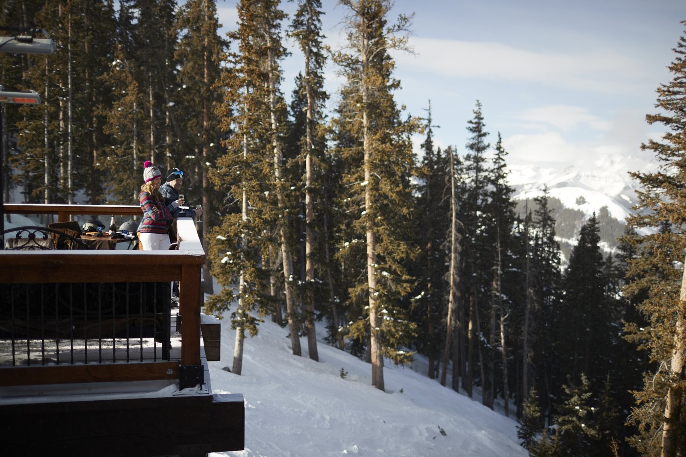 A couple with wine at the deck rail at Alpino Vino, looking out over the pines to the San Juan peaks, 11,966 feet above Telluride