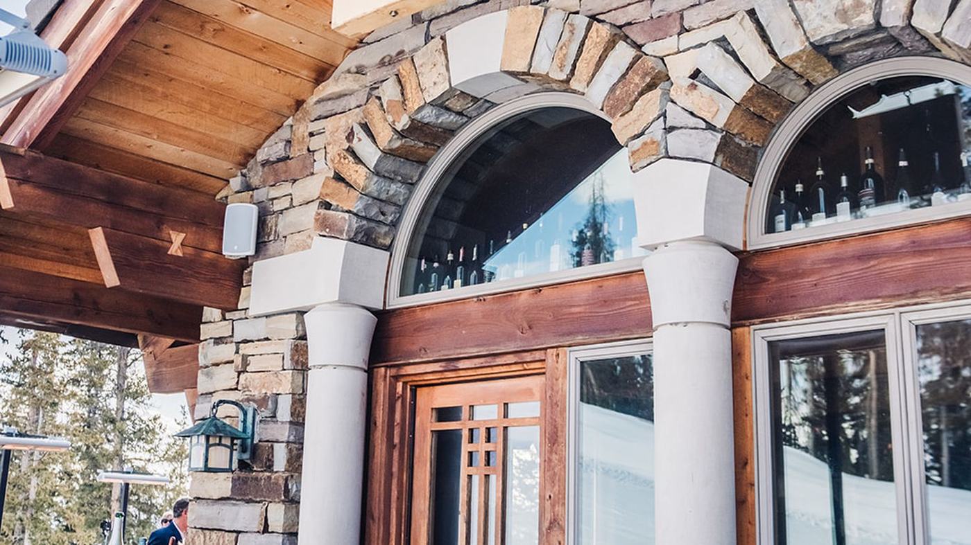 The carved Alpino Vino Wine Bar sign hanging beneath the timber eave, above the stone arches and the entrance to the restaurant at 11,966 feet