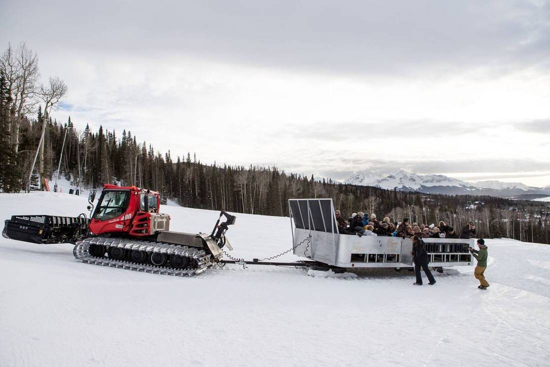 A snowcoach towing an open passenger coach full of wedding guests up the See Forever run to Alpino Vino, with the San Juan peaks behind, Telluride Ski Resort
