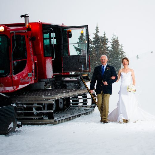 A bride arriving with her father beside the red Alpino Vino snowcoach in falling snow at Telluride Ski Resort