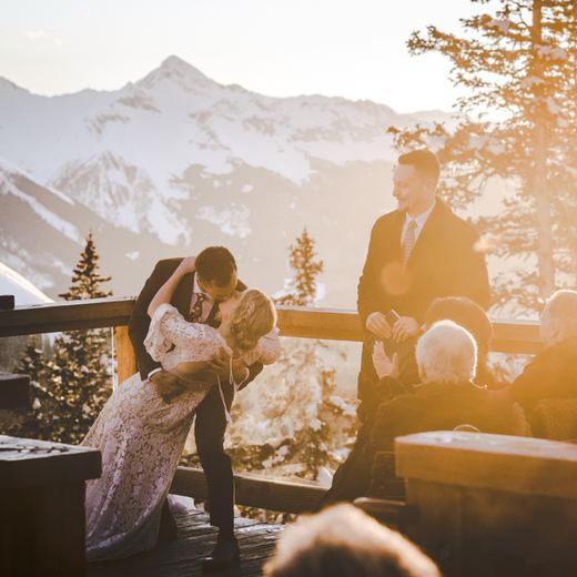 A newly married couple kissing on the Alpino Vino deck as the sun sets over the San Juan mountains, Telluride
