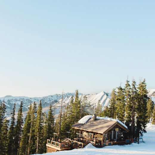 Alpino Vino seen from across the run in winter sun, the chalet and its deck among the pines with the San Juan peaks beyond