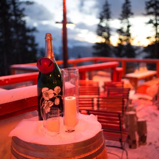 A magnum of champagne and candles on a snow-topped wine barrel on the Alpino Vino deck at dusk