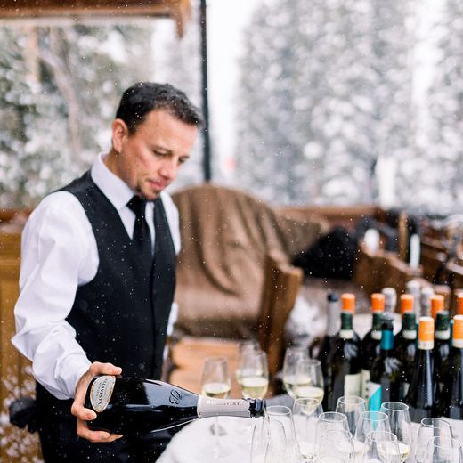 A server pouring champagne into a row of glasses on a snow-covered table on the Alpino Vino deck