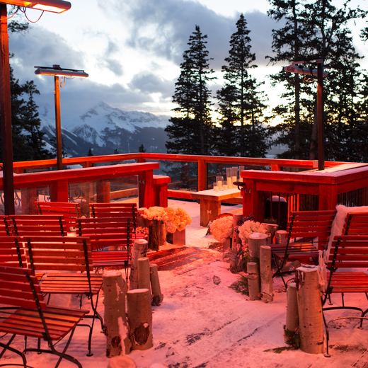The Alpino Vino ceremony deck at dusk under the glow of the overhead heaters, benches and blush florals with the peaks behind