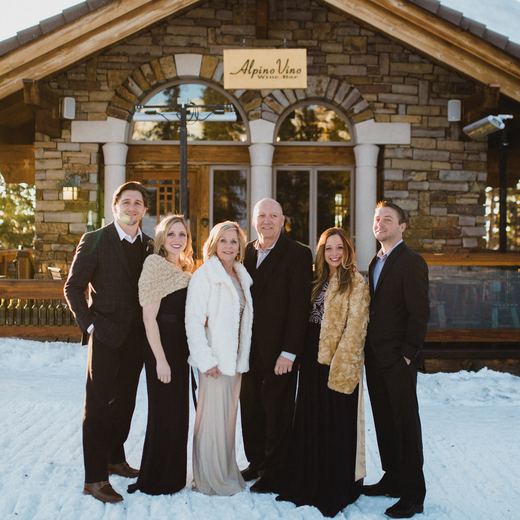 A family portrait in the snow outside Alpino Vino in evening light, the carved sign and stone arches behind them