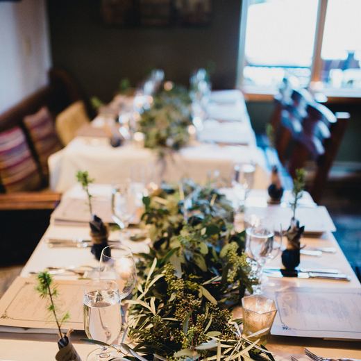 A long table at Alpino Vino dressed with a eucalyptus and olive runner, candles and printed menus