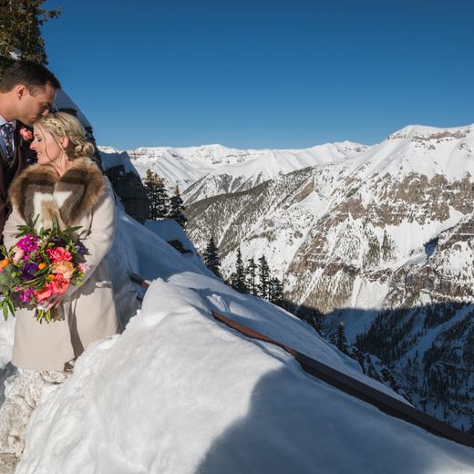 A couple on a snowy overlook above Telluride, the San Juan mountains falling away behind them