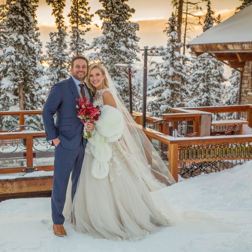 A bride and groom outside Alpino Vino at dusk, the snow-covered deck and chalet behind them