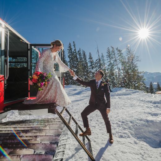 A groom helping his bride down the steps of the Alpino Vino snowcoach in bright winter sun at 11,966 feet above Telluride