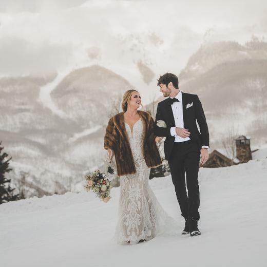 A bride and groom walking through deep snow on Gold Hill with the San Juan mountains behind, Telluride